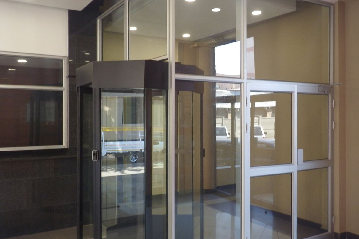 A modern building entrance lobby featuring a revolving glass door, aluminium framing, and polished granite wall finishes with recessed lighting.