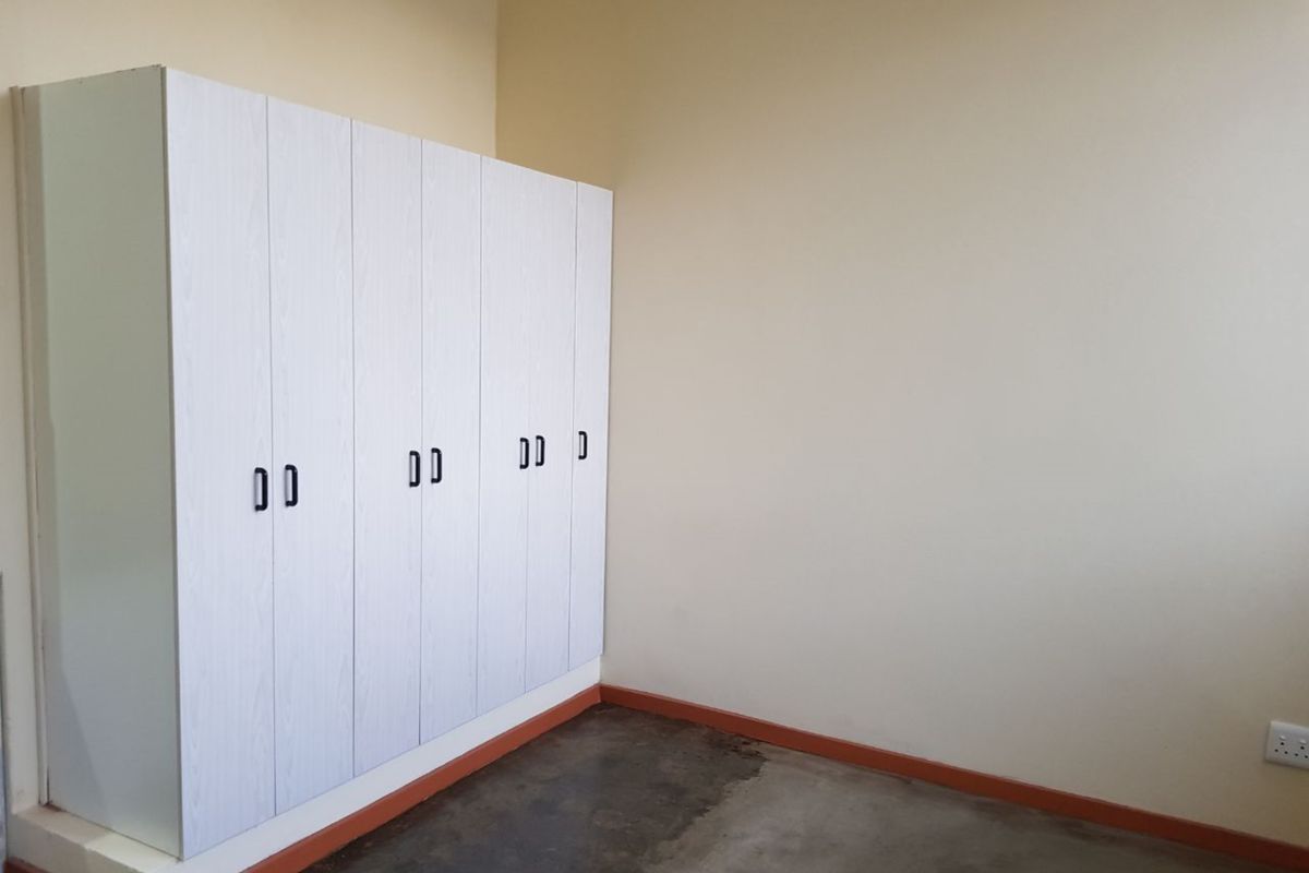 An empty bedroom featuring built-in white cupboards and concrete flooring with visible staining and dated skirting boards.