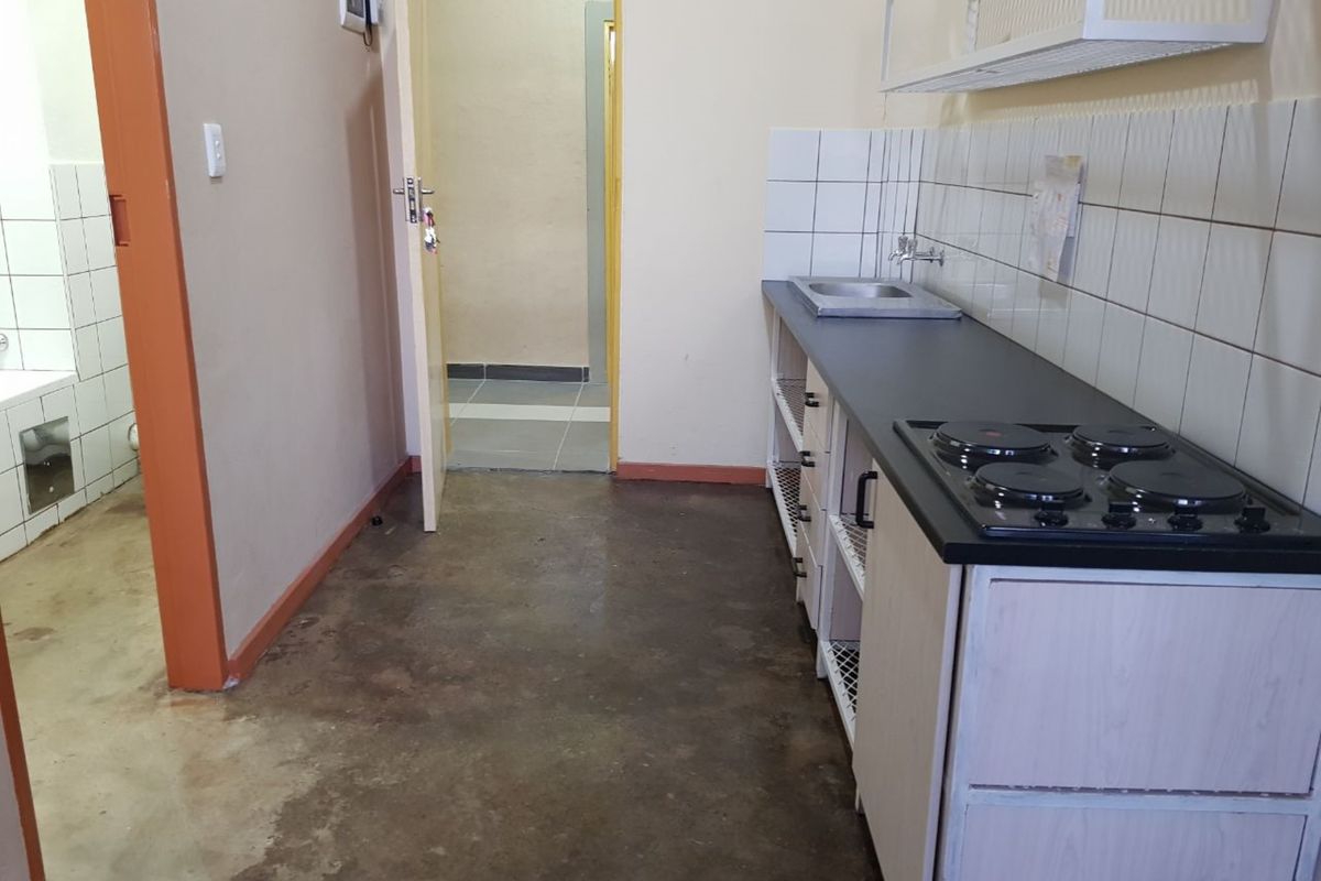 A compact, functional kitchen area featuring built-in cabinetry, an electric hob, and a stainless steel sink with tiled splashbacks.