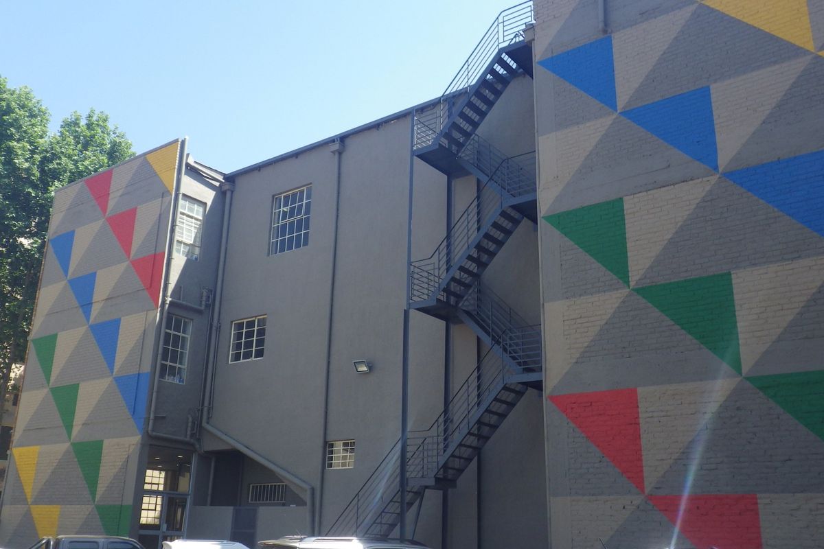 Rear elevation of the building featuring a painted geometric mural, external steel fire escape staircase, and multi-pane windows.
