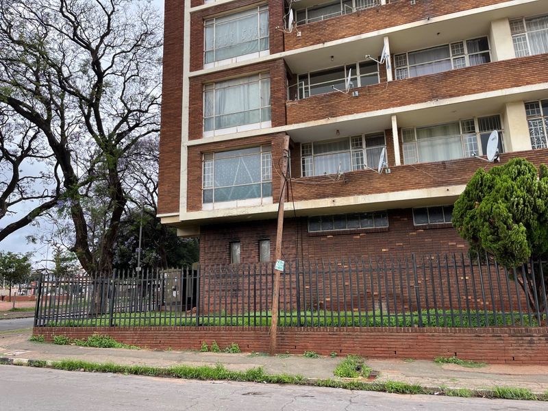 Exterior view of a multi-story brick apartment building featuring metal security fencing and multiple balconies with steel-framed windows.