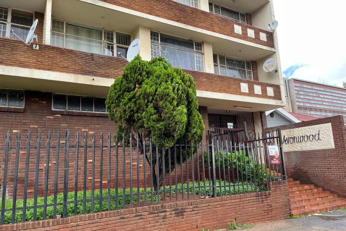 Front exterior view of a multi-story brick apartment building featuring metal security fencing, concrete stairs, and private balconies.