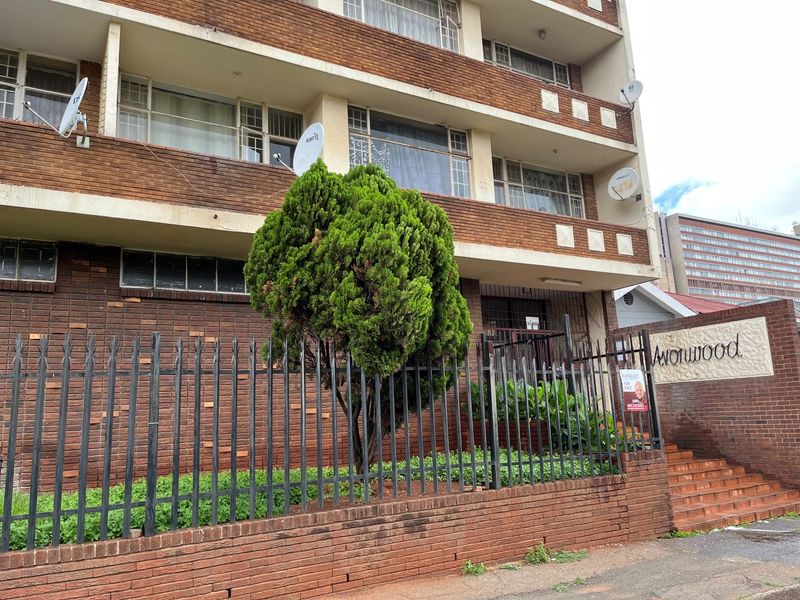 Front exterior view of a multi-story brick apartment building featuring metal security fencing, concrete stairs, and private balconies.