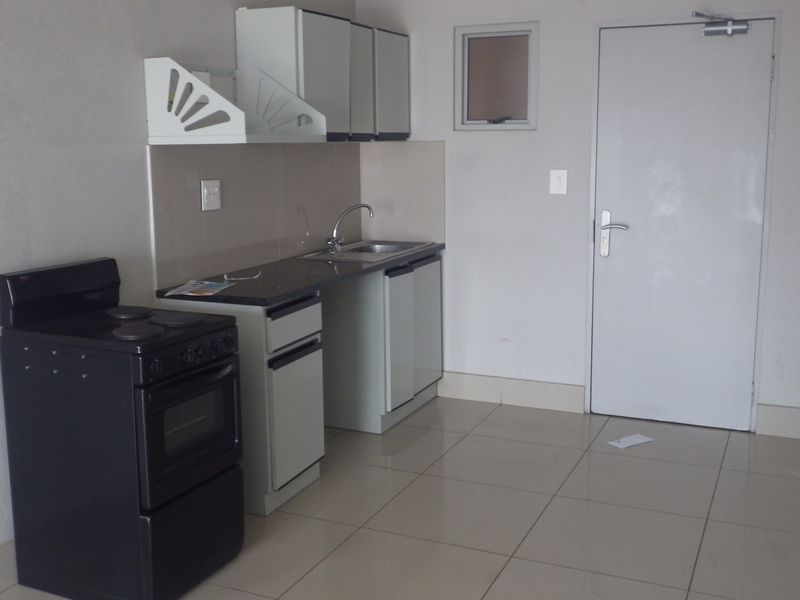 A compact, functional kitchen area featuring tiled flooring, built-in cabinetry, a stainless steel sink, and a freestanding stove.