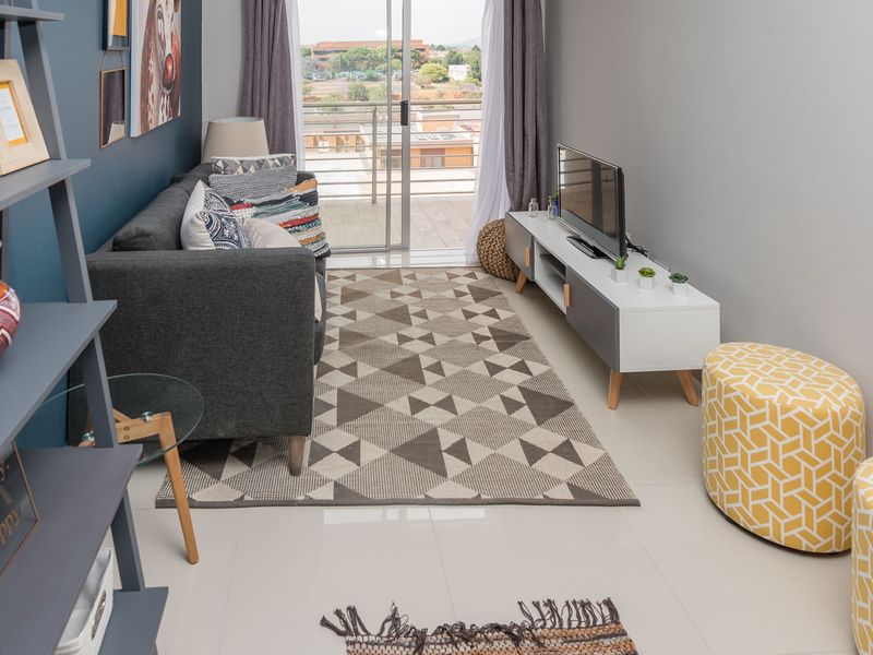 A well-maintained living room featuring tiled flooring, recessed ceiling lighting, and a sliding glass door providing access to an outdoor balcony.