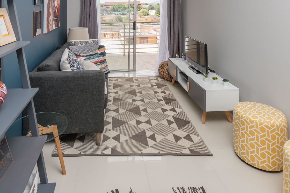 A well-maintained living room featuring tiled flooring, recessed ceiling lighting, and a sliding glass door providing access to an outdoor balcony.
