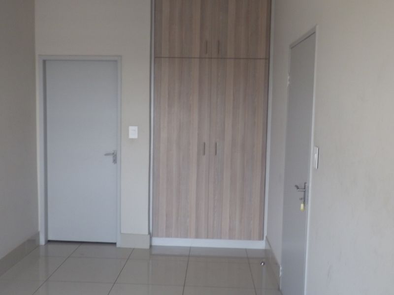 A clean, empty bedroom featuring neutral tiled flooring and modern built-in wooden cupboards with ample storage space.