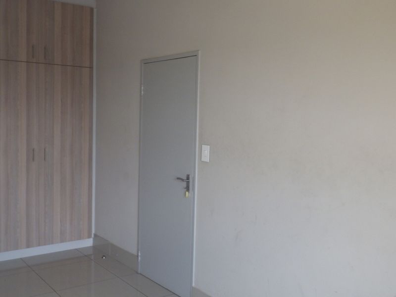 A clean, empty bedroom featuring neutral tiled flooring and built-in wooden cupboards, providing a blank canvas for personalization.