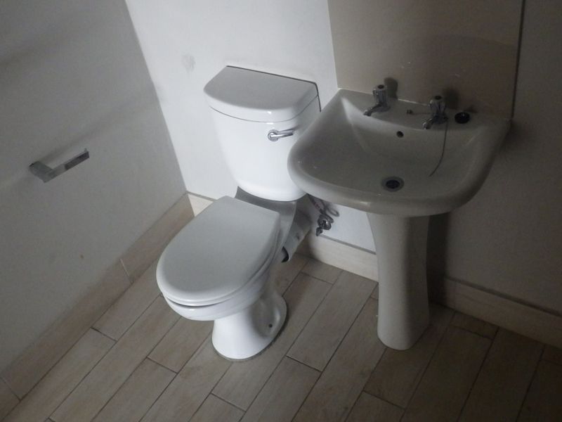 A functional bathroom featuring a pedestal basin, toilet, and tiled flooring, providing a clean and simple layout.