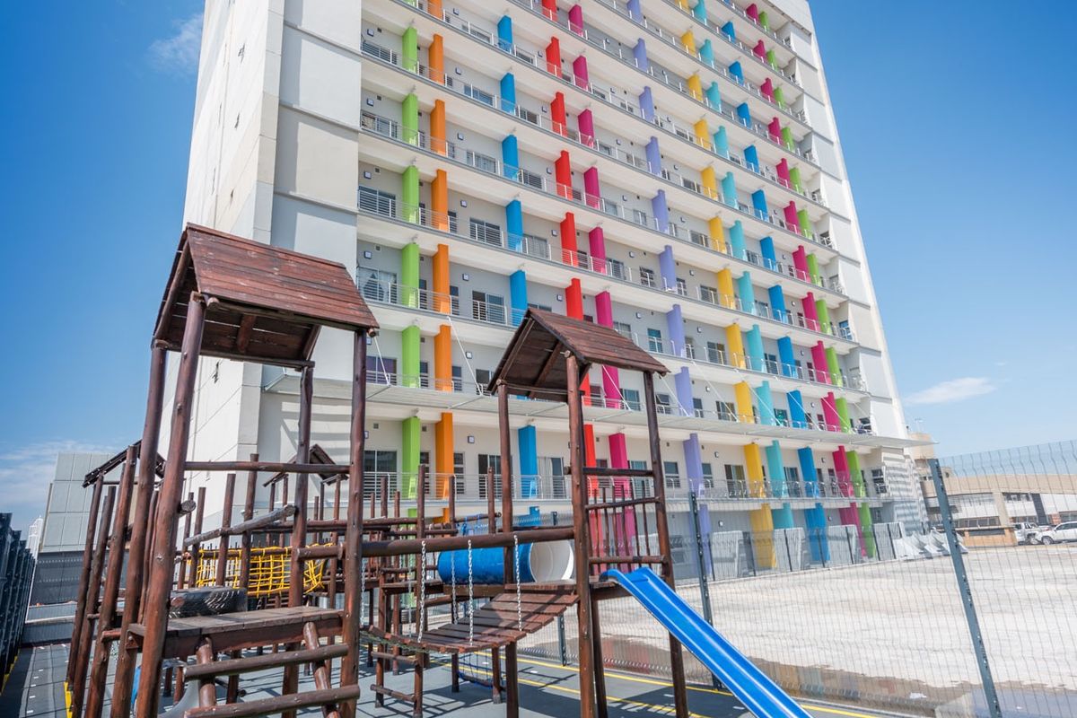 Exterior view of a multi-story apartment building featuring a colorful facade and an adjacent outdoor playground area with fixed play structures.