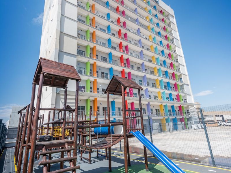 Exterior view of a multi-story apartment building featuring a colorful facade and an adjacent outdoor playground area with fixed play structures.