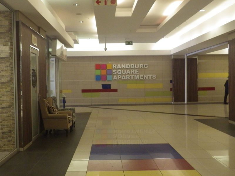 A modern, well-lit entrance lobby for Randburg Square Apartments featuring tiled floors, recessed ceiling lighting, and decorative wall paneling.