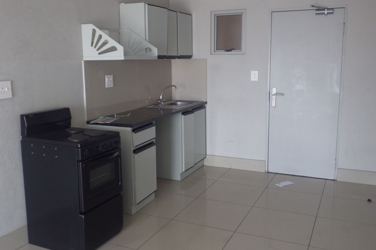 A compact, empty kitchen featuring basic cabinetry, a sink, a freestanding stove, and tiled flooring, providing a functional space ready for personalization.
