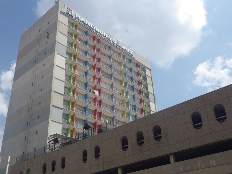 Exterior view of Randburg Square, a multi-story residential building featuring colorful facade accents and an adjacent parking structure.