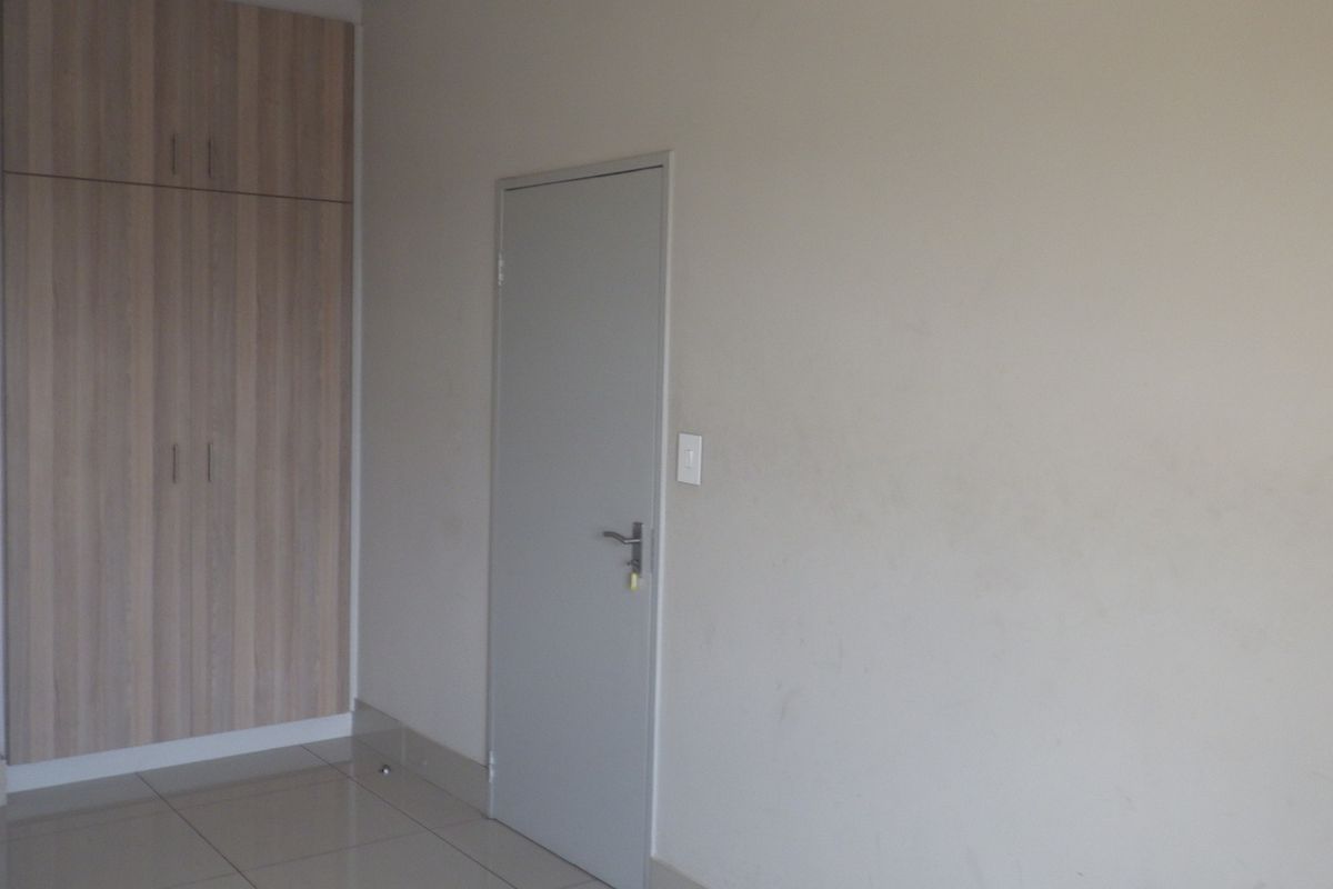 A clean, empty bedroom featuring neutral tiled flooring and built-in wooden cupboards, providing a blank canvas for personalization.