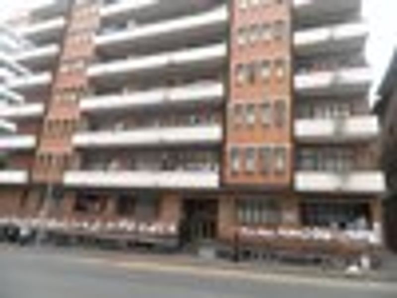 A multi-story brick apartment building featuring multiple balconies and a street-level entrance.