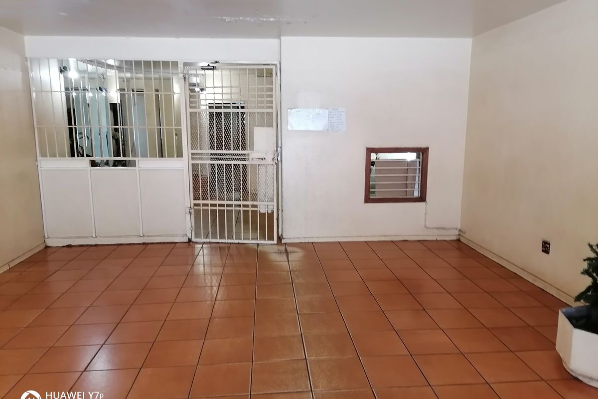 An empty interior space featuring terracotta floor tiles, a security gate entrance, and a small fixed window.
