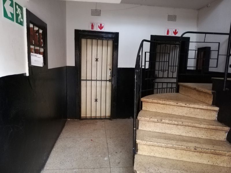 A communal hallway area featuring a staircase with metal handrails, security gates, and fire safety signage in a functional apartment building setting.