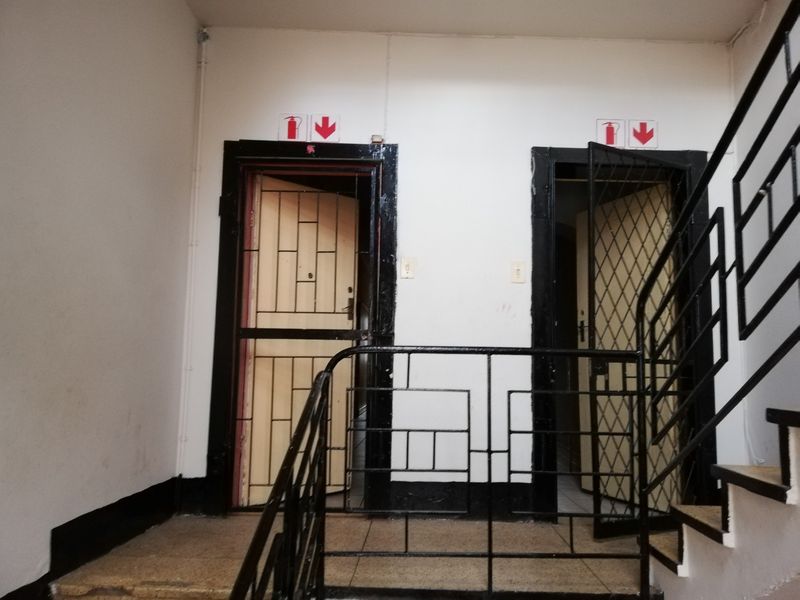 A communal hallway area featuring metal security gates, staircase railings, and fire safety signage, showing signs of wear and tear.