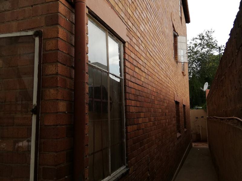A narrow side passage of the flat featuring face brick exterior walls, a concrete pathway, and a downpipe along the building facade.