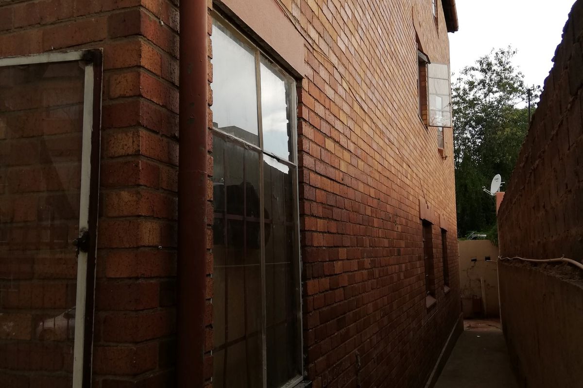 A narrow side passage of the flat featuring face brick exterior walls, a concrete pathway, and a downpipe along the building facade.