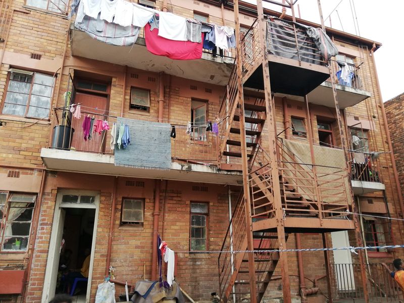 Rear elevation of a multi-story brick apartment building featuring external steel staircases and concrete balconies with visible signs of wear and weathering.
