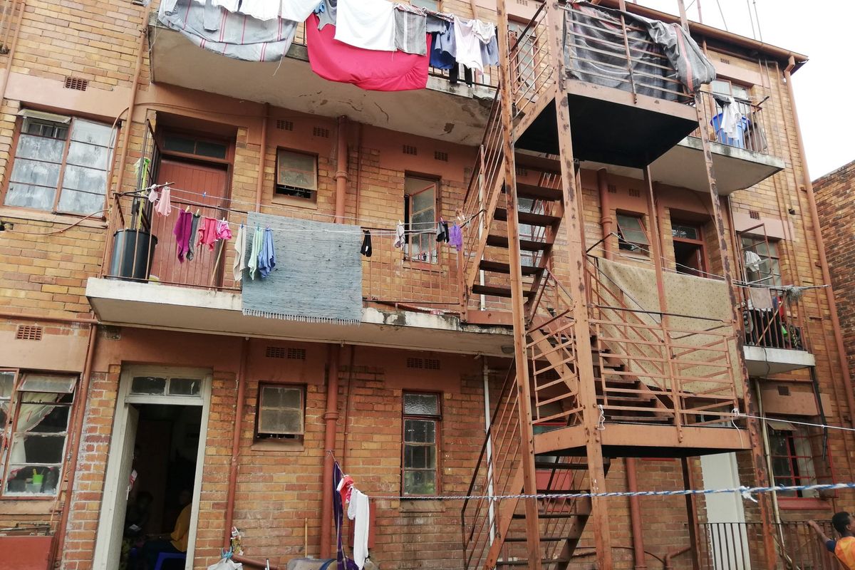 Rear elevation of a multi-story brick apartment building featuring external steel staircases and concrete balconies with visible signs of wear and weathering.