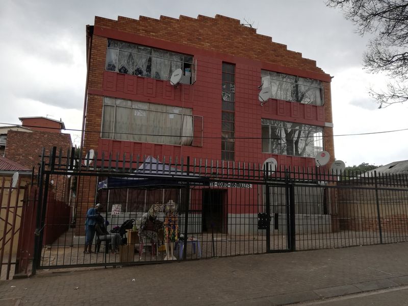 Front elevation of a multi-story brick apartment building featuring metal security fencing and multiple satellite dish installations.