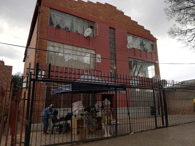 Front elevation of a multi-story brick apartment building featuring large windows and a secure metal perimeter fence.
