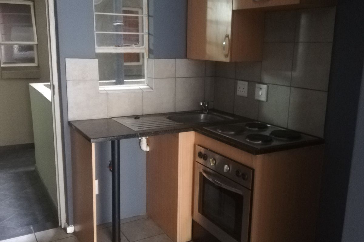 Compact kitchen featuring built-in cabinetry, a stove with oven, and tiled flooring, requiring some maintenance and cosmetic updates.